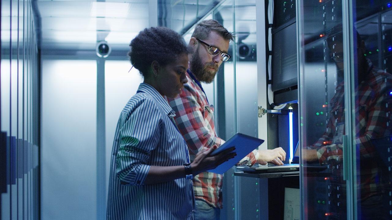 Two people, a man and a woman, are logged into a terminal in a data center data hall